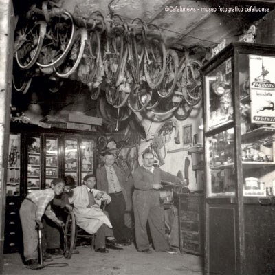 1960 Totò Maggio in primo piano nel suo laboratorio di Via Matteotti , dietro a lui inn piedi il macellaio Pasquale Guercio, seduto il barbiere Pino Portera , seguono due ragazzini che gonfiano le ruote di una bici . Notiamo dalla foto le bici appese nel tetto dell’officina 